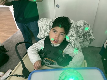 boy in adaptive seating using a switch to activate a sensory toy