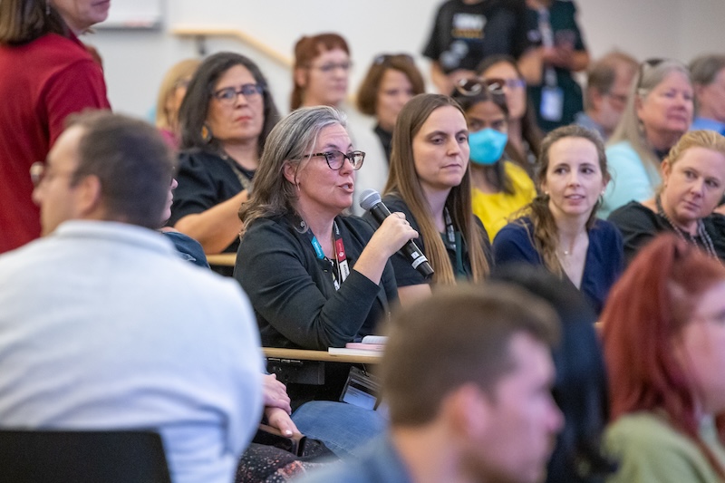 Woman sitting in audience asking questions to chancellor using a microphone