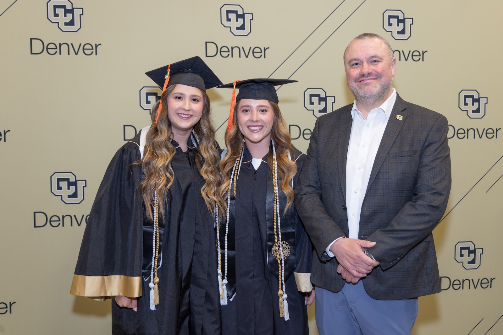 Chancellor Christensen stands next to two spring 2025 graduates.