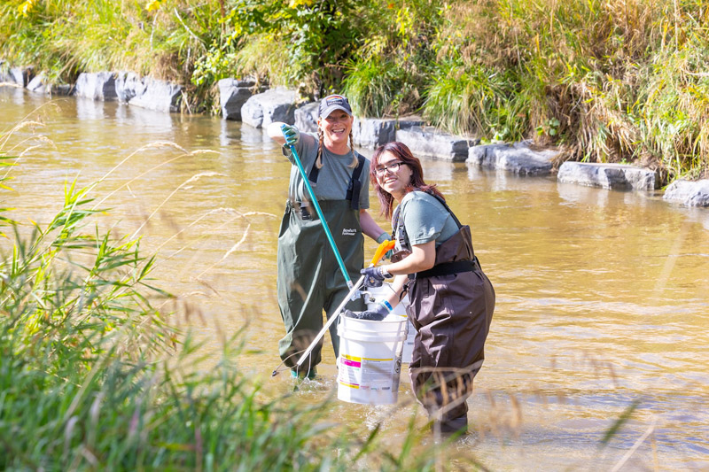 Two people clean up trash in Cherry Creek.