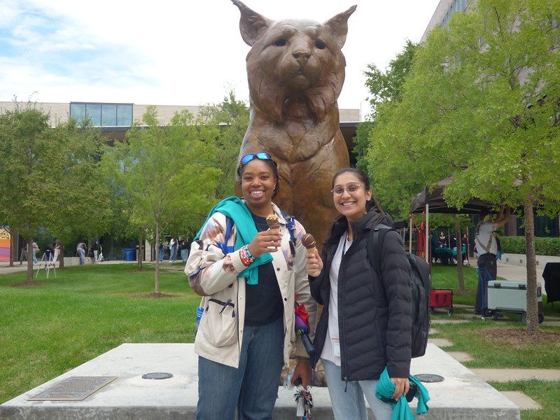 Two women standing in front of a bronze Lynx statue