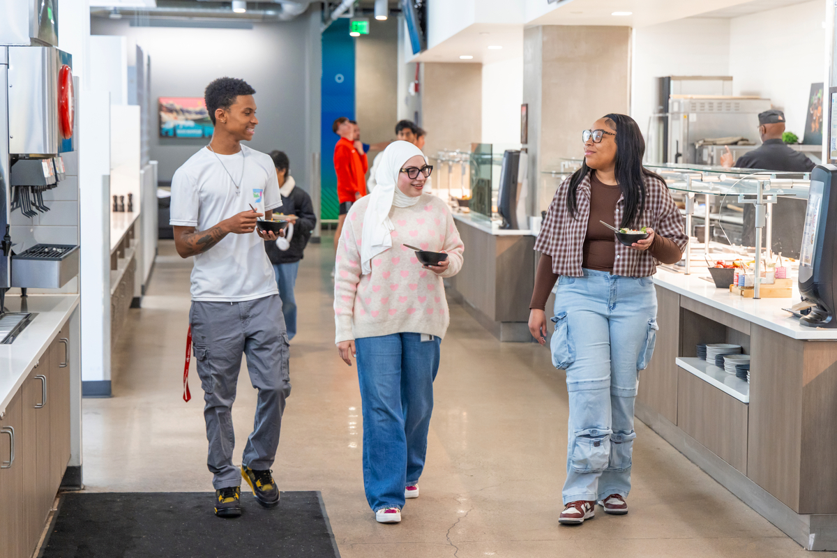 three students walking through the dining hall holding plates