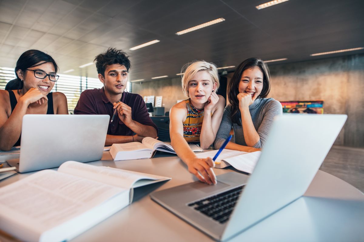 group of 4 people sitting at a table and looking at a laptop studying