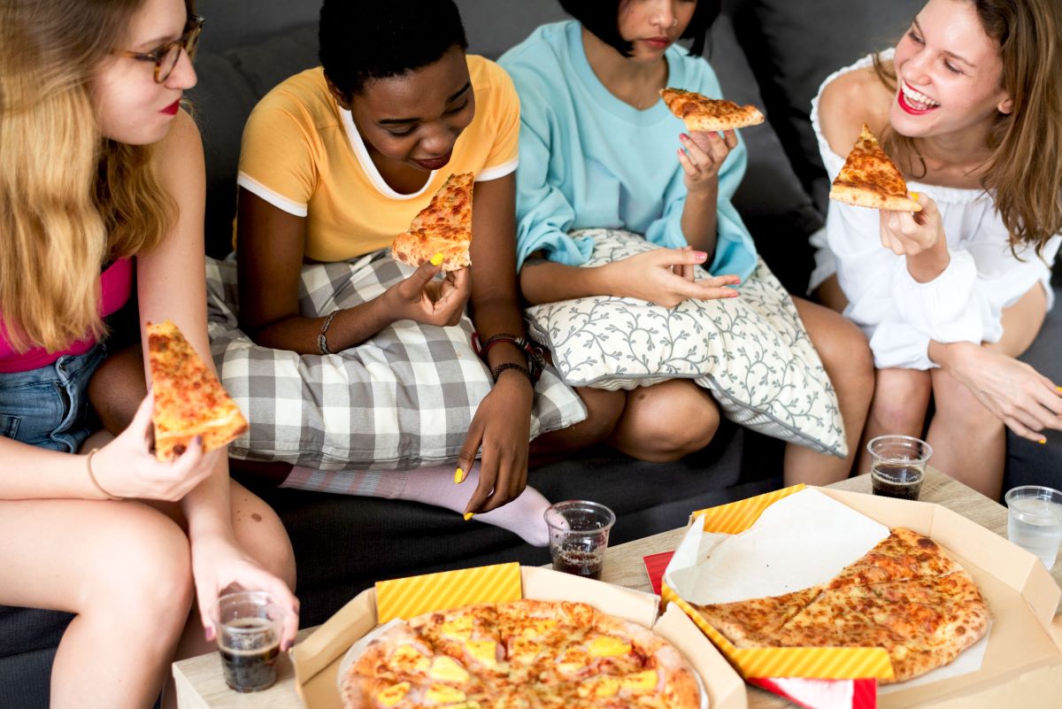 4 people eating pizza sitting with pillows on their laps