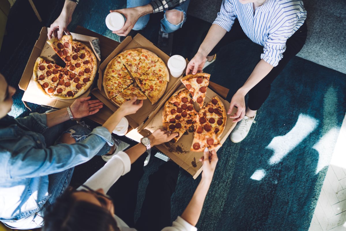 birdseye view of three pizzas and people grabbing a slice